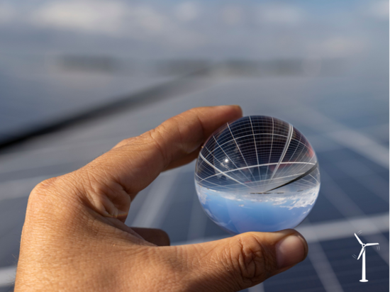 Eine Hand hält eine kleine Glaskugel, in der sich der Himmel und Solaranlagen spiegeln | © canva