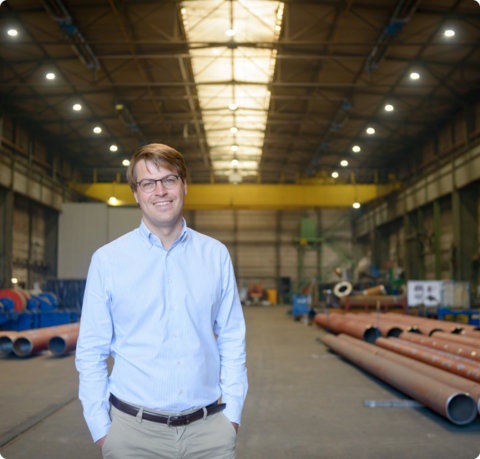Julius Kramer, Urenkel des Firmengründers und seit 2016 geschäftsführender Gesellschafter der J. Heinr .Kramer Gruppe | © Antje Schimanke/Gedankenwerft Mann mit Brille lächelt in die Kamera, im Hintergrund sieht man eine Lagerhalle | © Antje Schimanke/Gedankenwerft