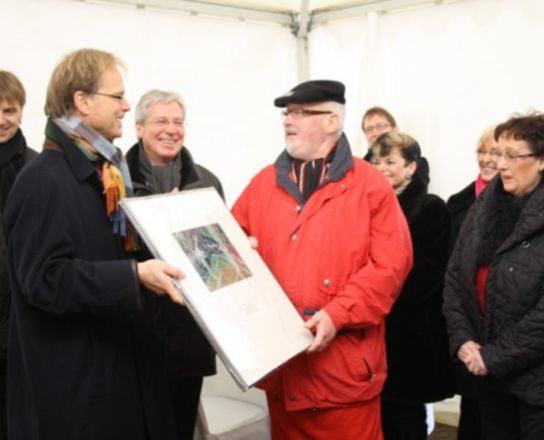 Festakt zur Gebietsübertragung | © Wilfried Moritz/Magistrat der Stadt Bremerhaven Ein Mann überreicht einem anderen Mann einen Bilderrahmen. Im Hintergrund stehen weitere Menschen. | © Wilfried Moritz/Magistrat der Stadt Bremerhaven