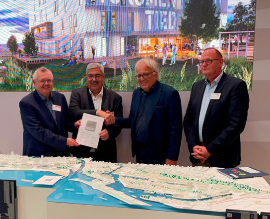 Überreichung Platin-Vorzertifikat von der DGNB für das Gründungszentrum auf der Expo Real | © BIS Bremerhaven Vier Männer lächeln in die Kamera vor einem Stadtmodell. Zwei der Männer halten einen DinA4 großen Zettel in die Kamera. Im Hintergrund ist eine Leinwand. | © BIS Bremerhaven